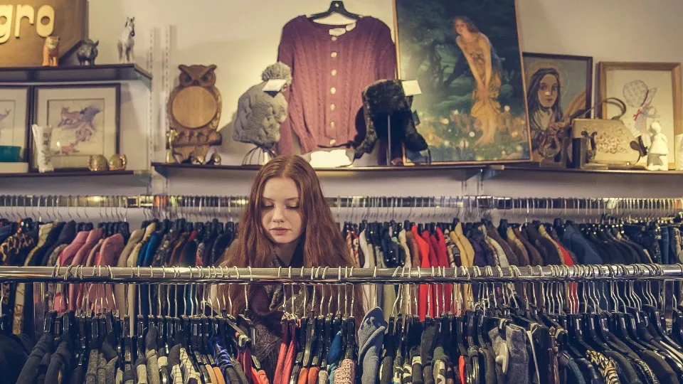 Shopper browsing a packed rack of secondhand clothes in a thrift store